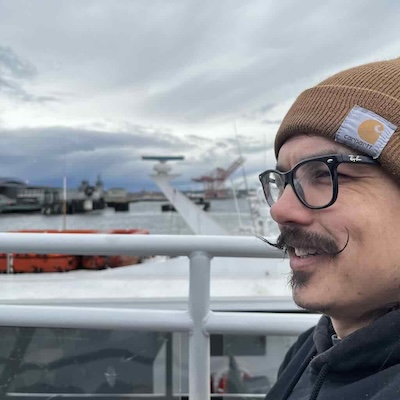 A profile picture of Jason at seattle's waterfront. He has a large handlebar mustache and is wearing a brown beanie